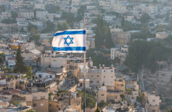 Israeli National flag waving on the top of Mount of Olive with background of residential houses in Jerusalem, Israel